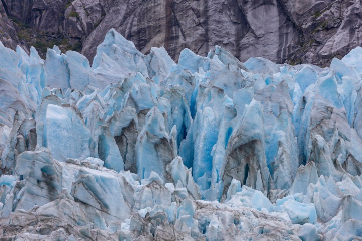 Close-up view of a jagged, blue glacier with rocky background.