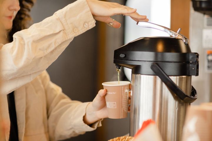 Person dispensing beverage from a thermal coffee server into a cup.