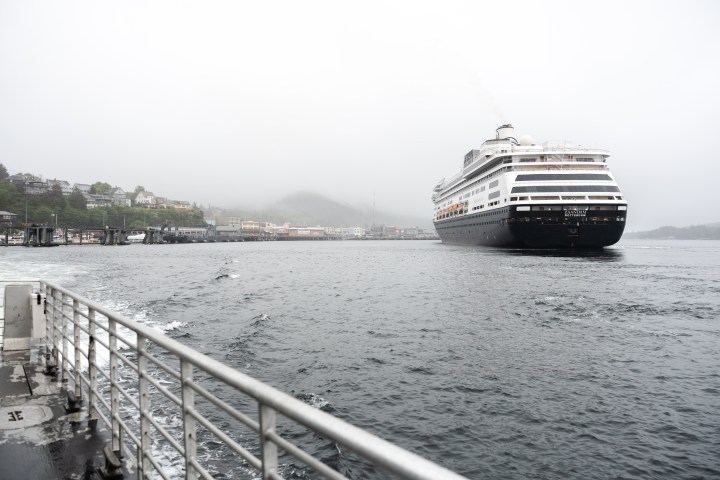 Cruise ship docked in misty harbor with town and hills in background.