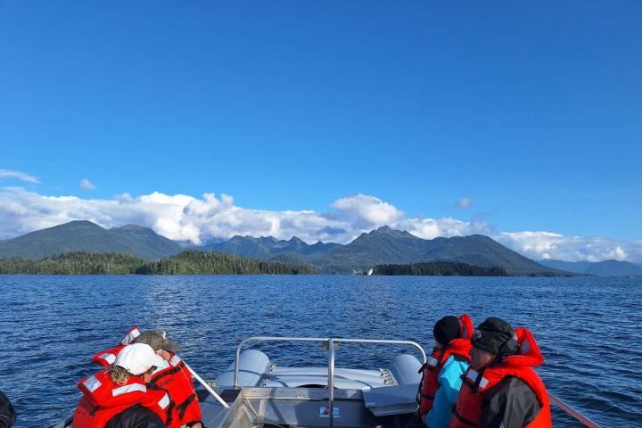 People in red life jackets sit on a boat with mountains in the background.