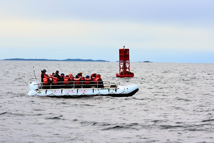 Boat with people in life jackets near a red buoy on the ocean.