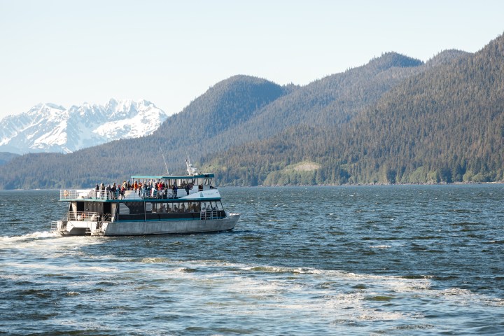 Tour boat with passengers on a lake, mountains in the background.
